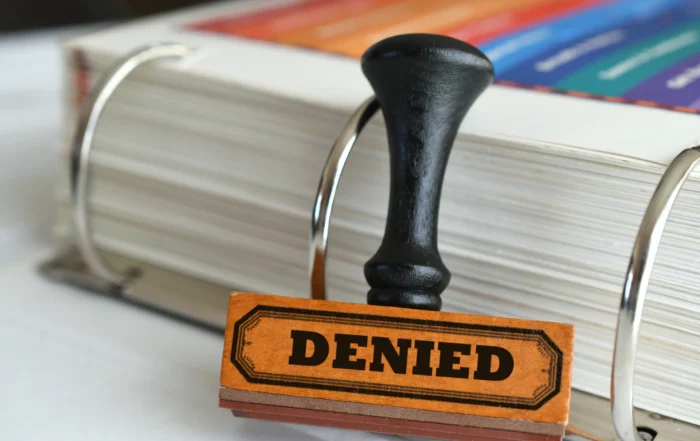 Rubber stamp marked “DENIED” resting on an open binder filled with documents, symbolizing a rejected SSDI claim and the disability appeals process after multiple denials in Louisiana.